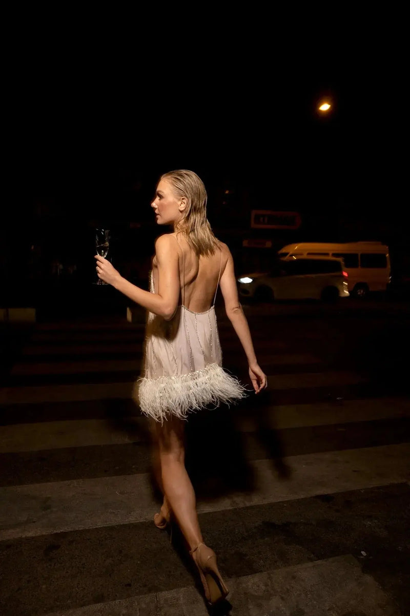 Woman in a white feathered dress walking at night with a blurred background