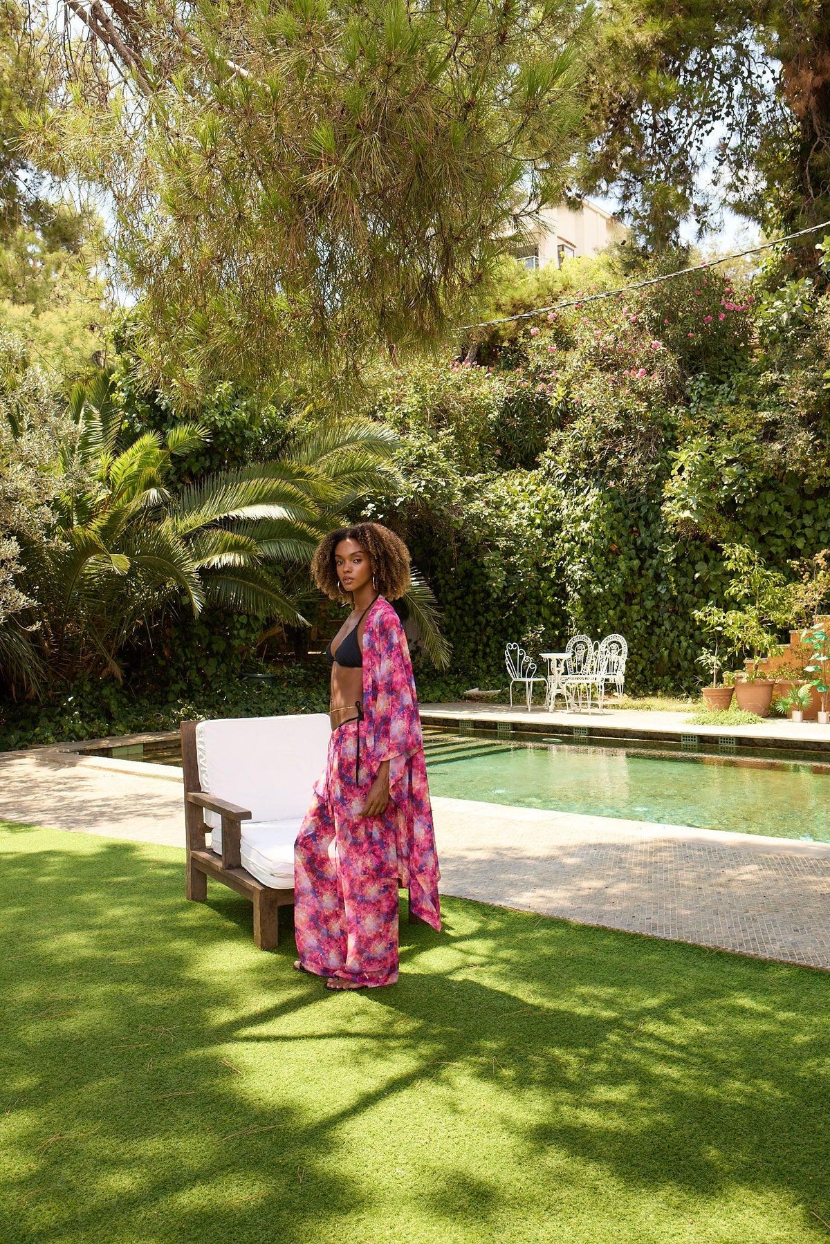 Woman in a colorful dress standing by a pool with greenery in the background