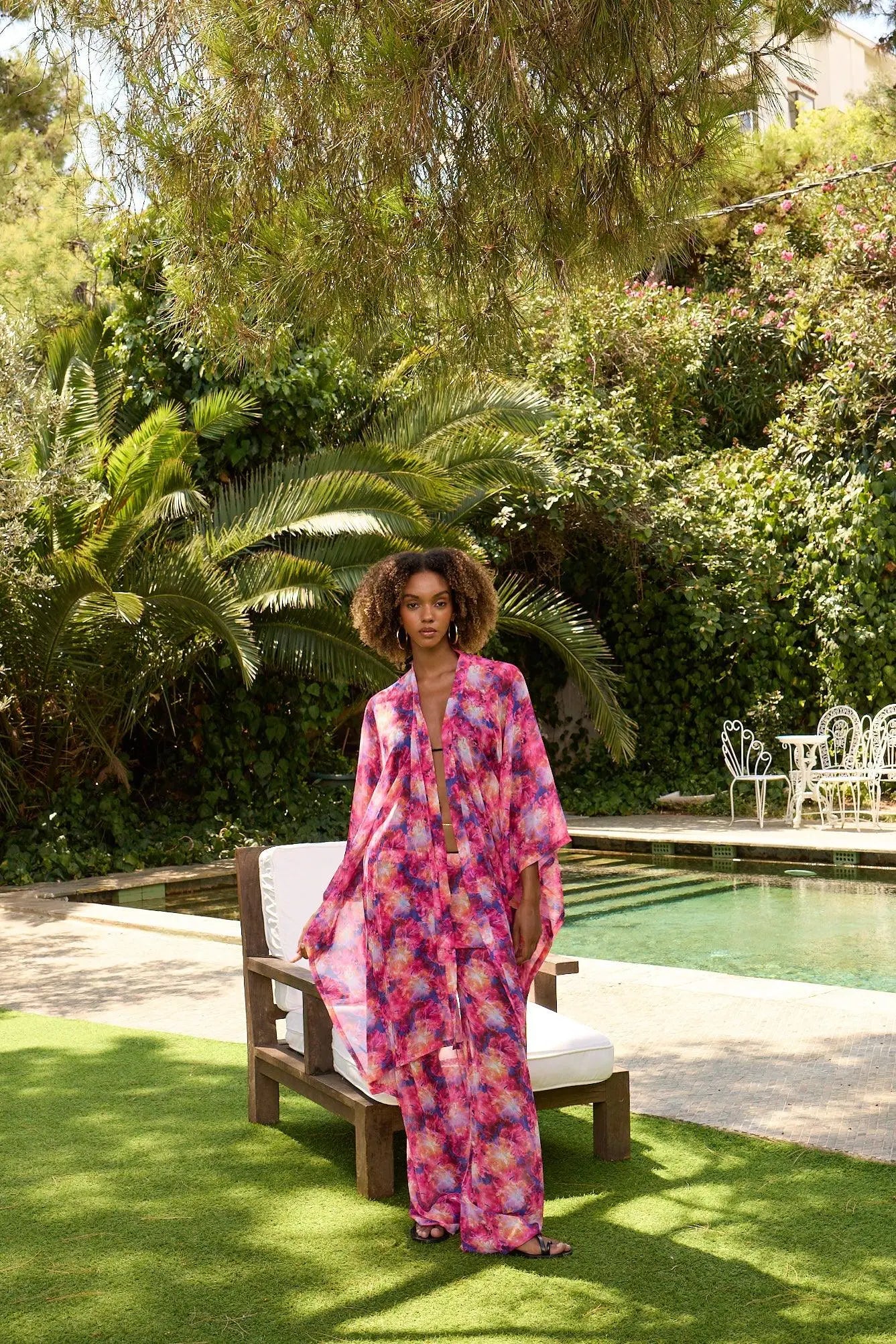 Woman in a colorful dress standing by a pool with greenery in the background