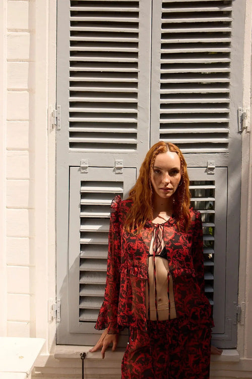 Woman in a red floral outfit standing in front of gray shutters.
