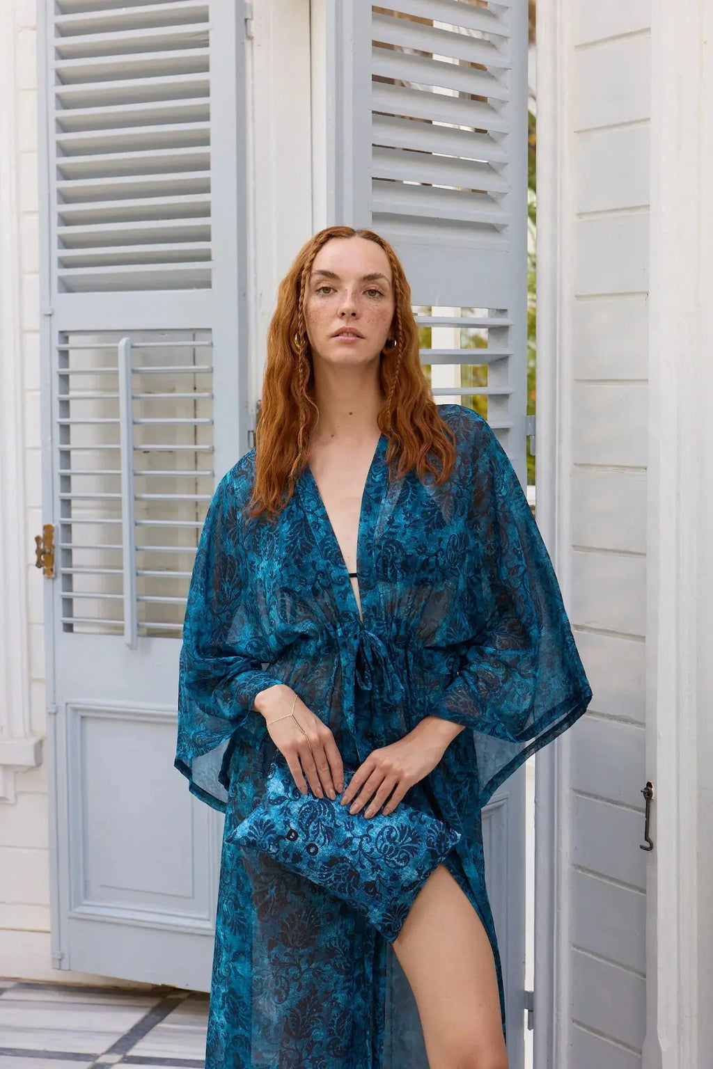 Woman wearing a blue floral dress standing in front of a white door.