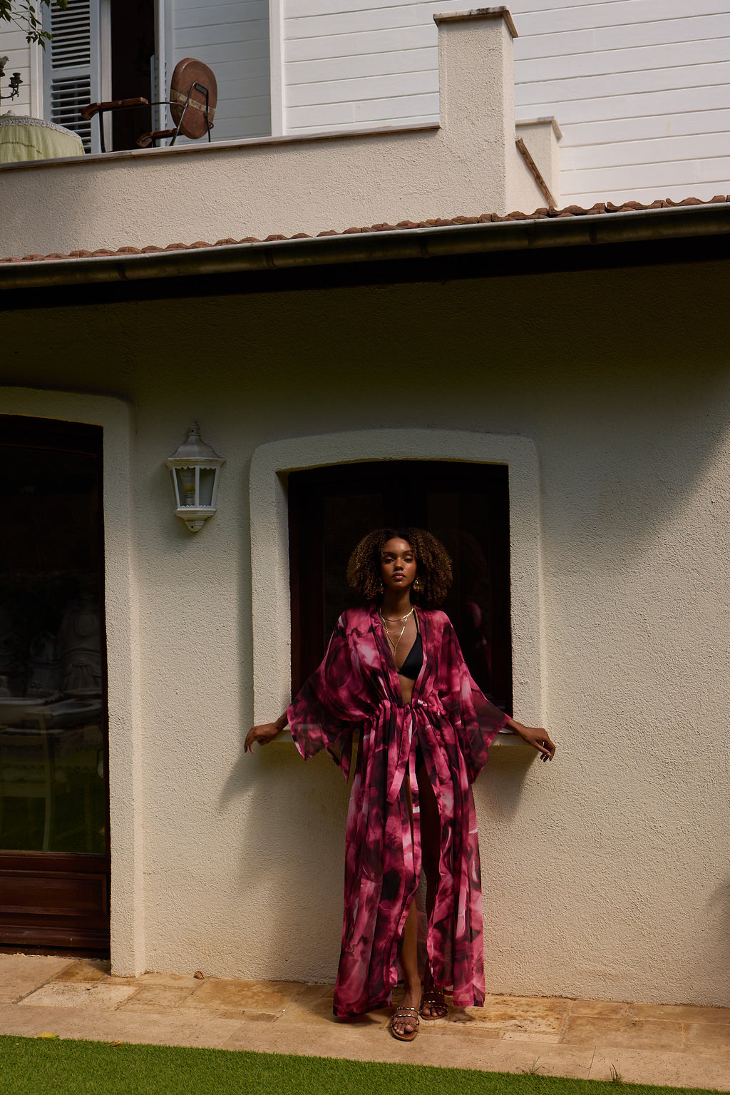 Woman in a pink and purple patterned dress standing in front of a house.