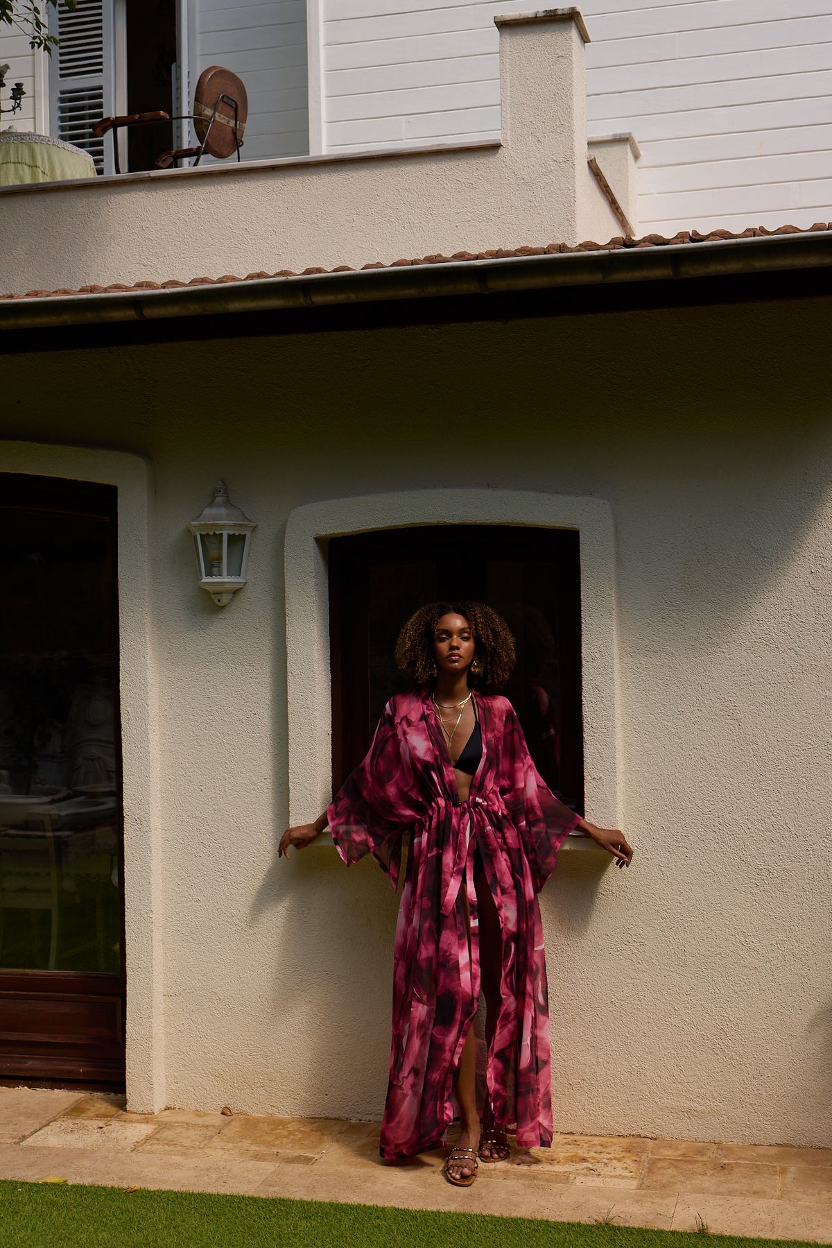 Woman in a pink and purple patterned dress standing in front of a house.