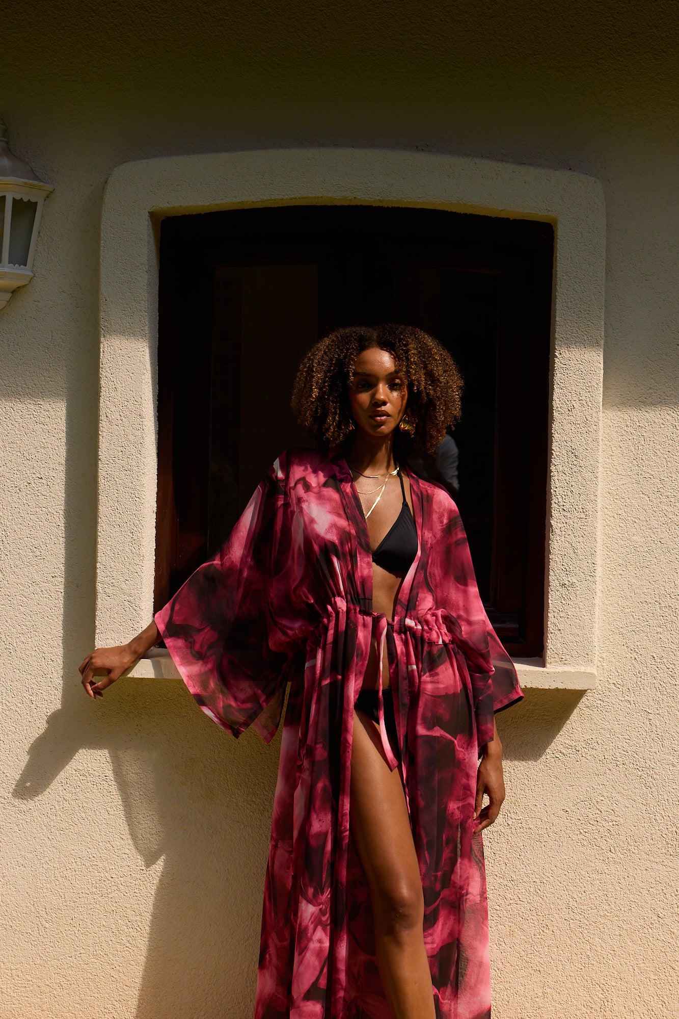 Woman in a pink and black patterned robe standing in front of a window.