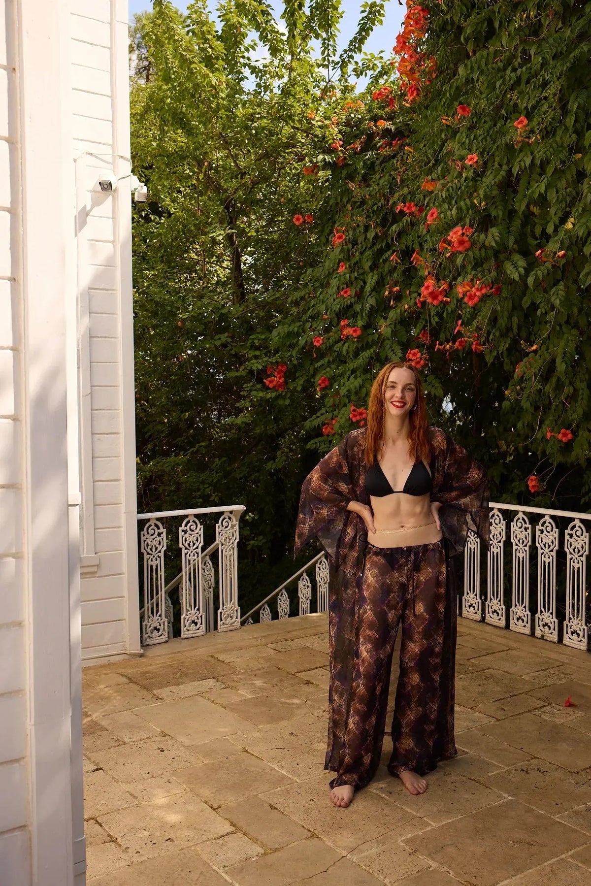 Woman standing on a stone patio with a white building and greenery in the background