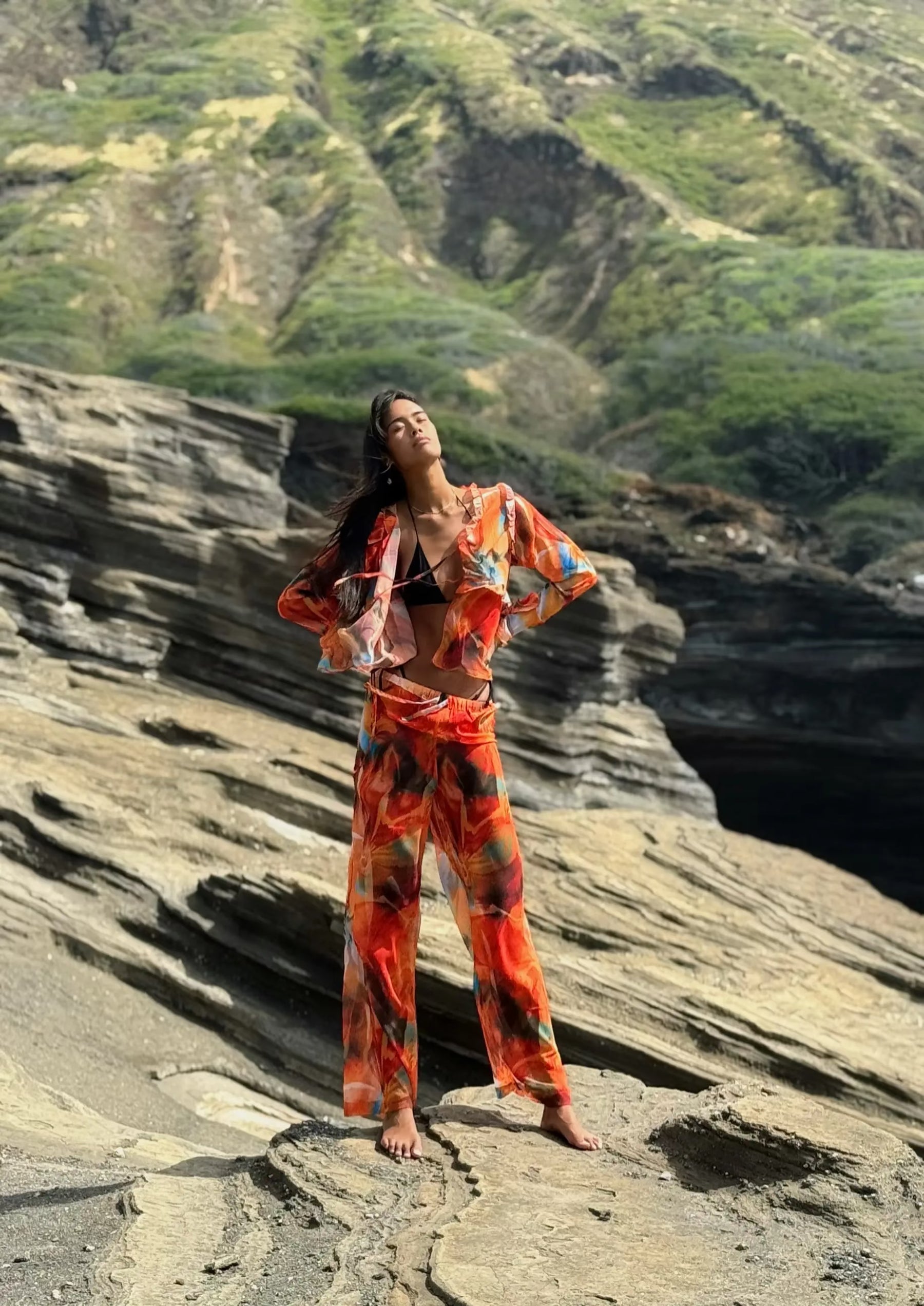 Person wearing a colorful outfit standing on a rocky cliff with greenery in the background