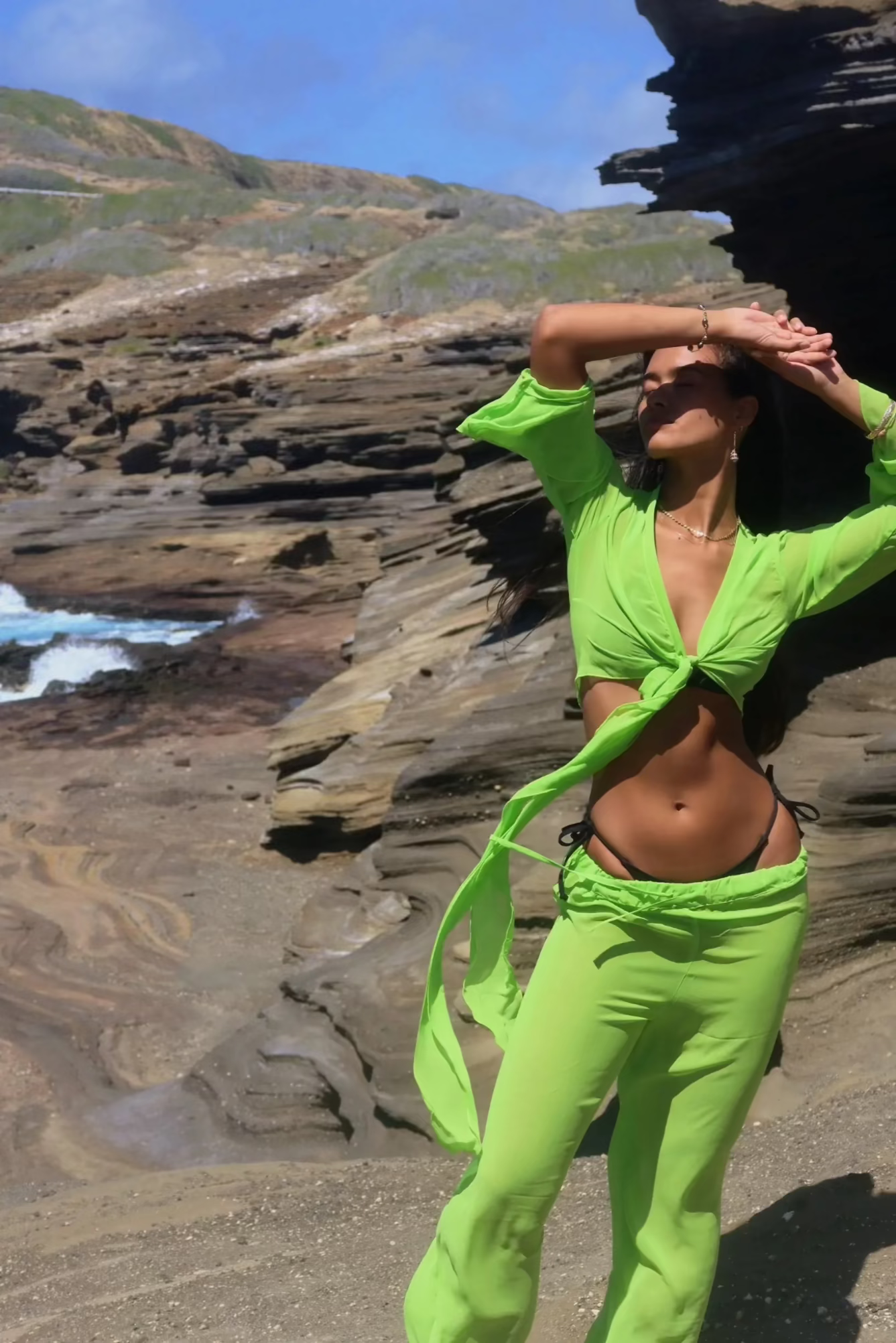 Person wearing a bright green outfit standing on a rocky beach.