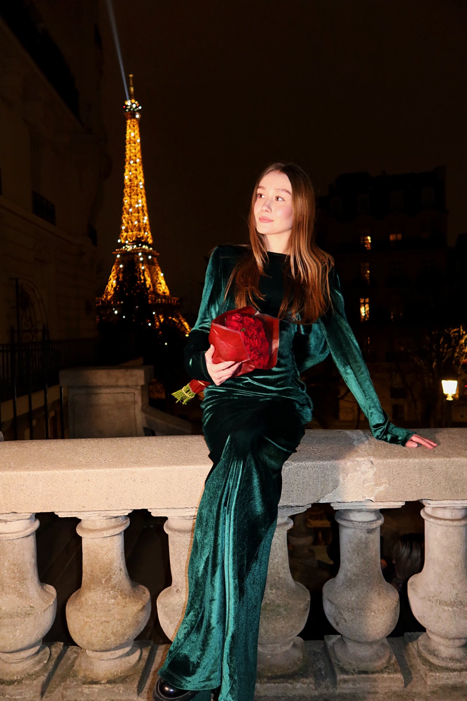 Woman in a green velvet outfit holding a red bag with the Eiffel Tower in the background