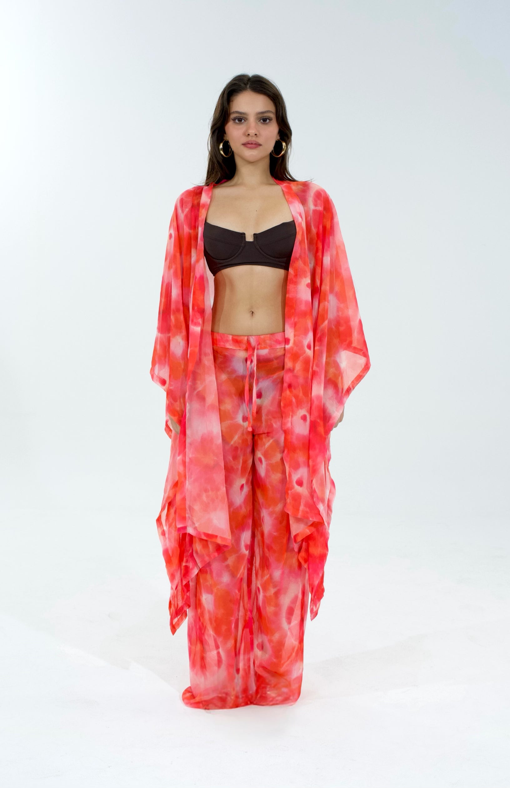 Woman wearing a red and white patterned kimono over a black top and pink pants on a white background