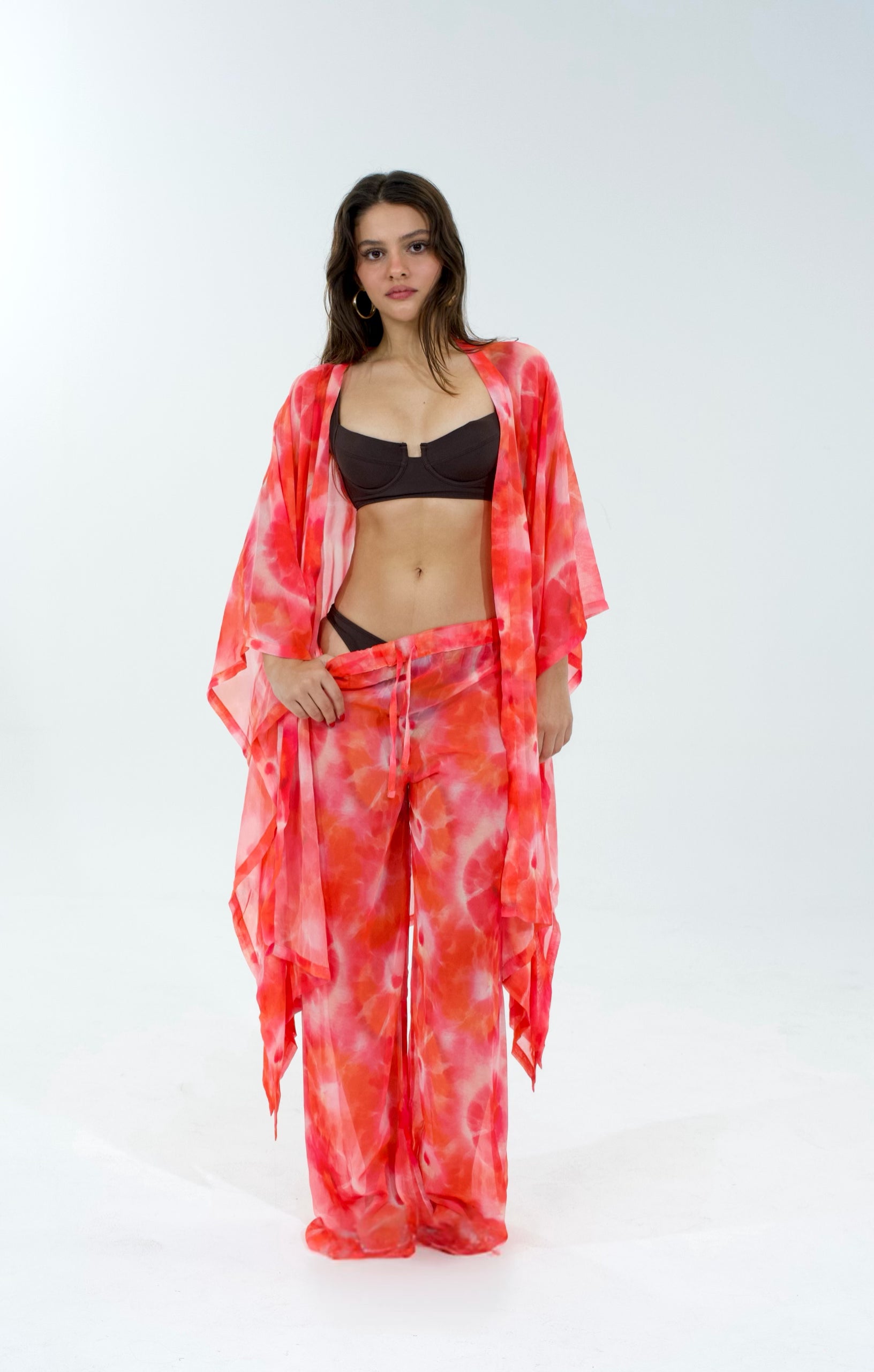 Woman wearing a red tie-dye kimono over a black bikini on a white background