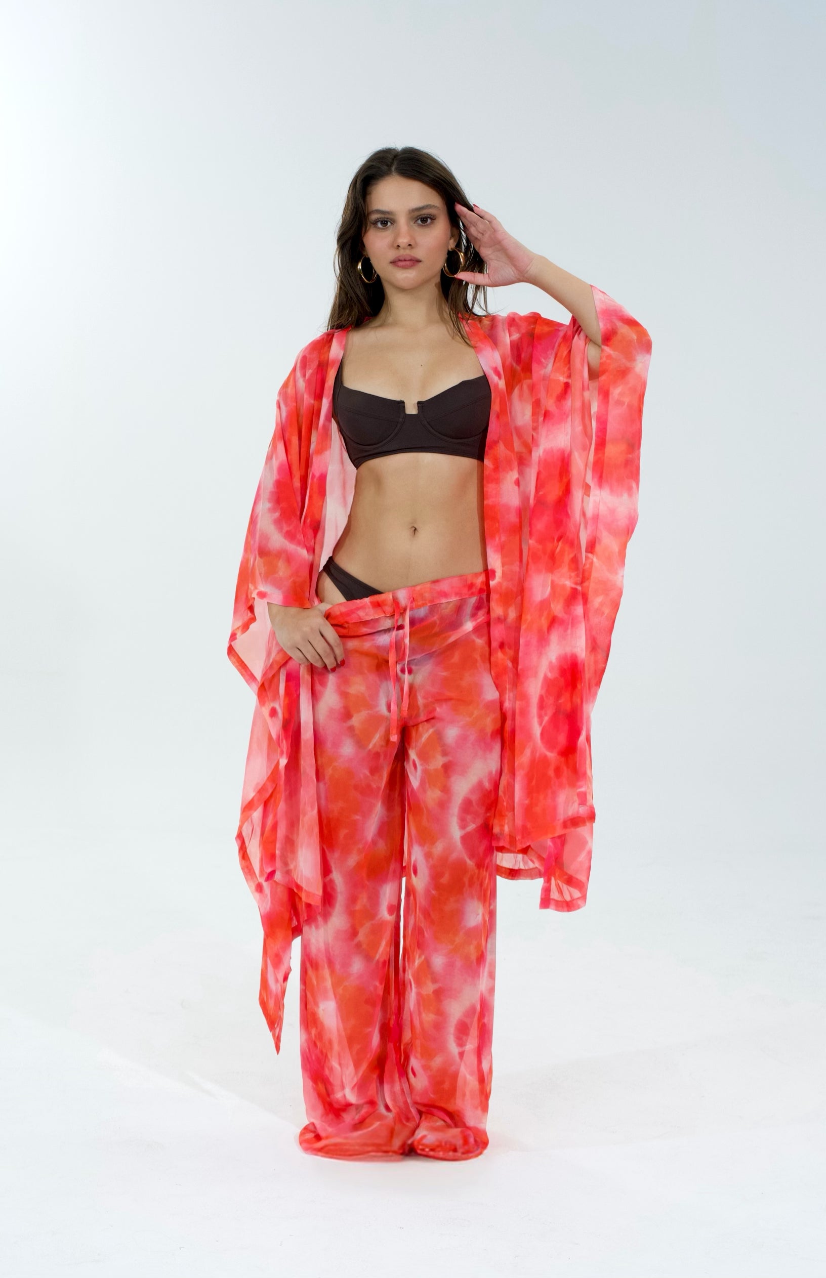 Woman wearing a red tie-dye kimono over a black bikini on a white background
